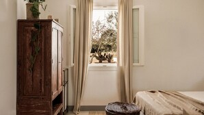 Una habitación con un armario de madera, una cesta de mimbre, dos camas con cubrecamas color beige y una ventana con cortinas.