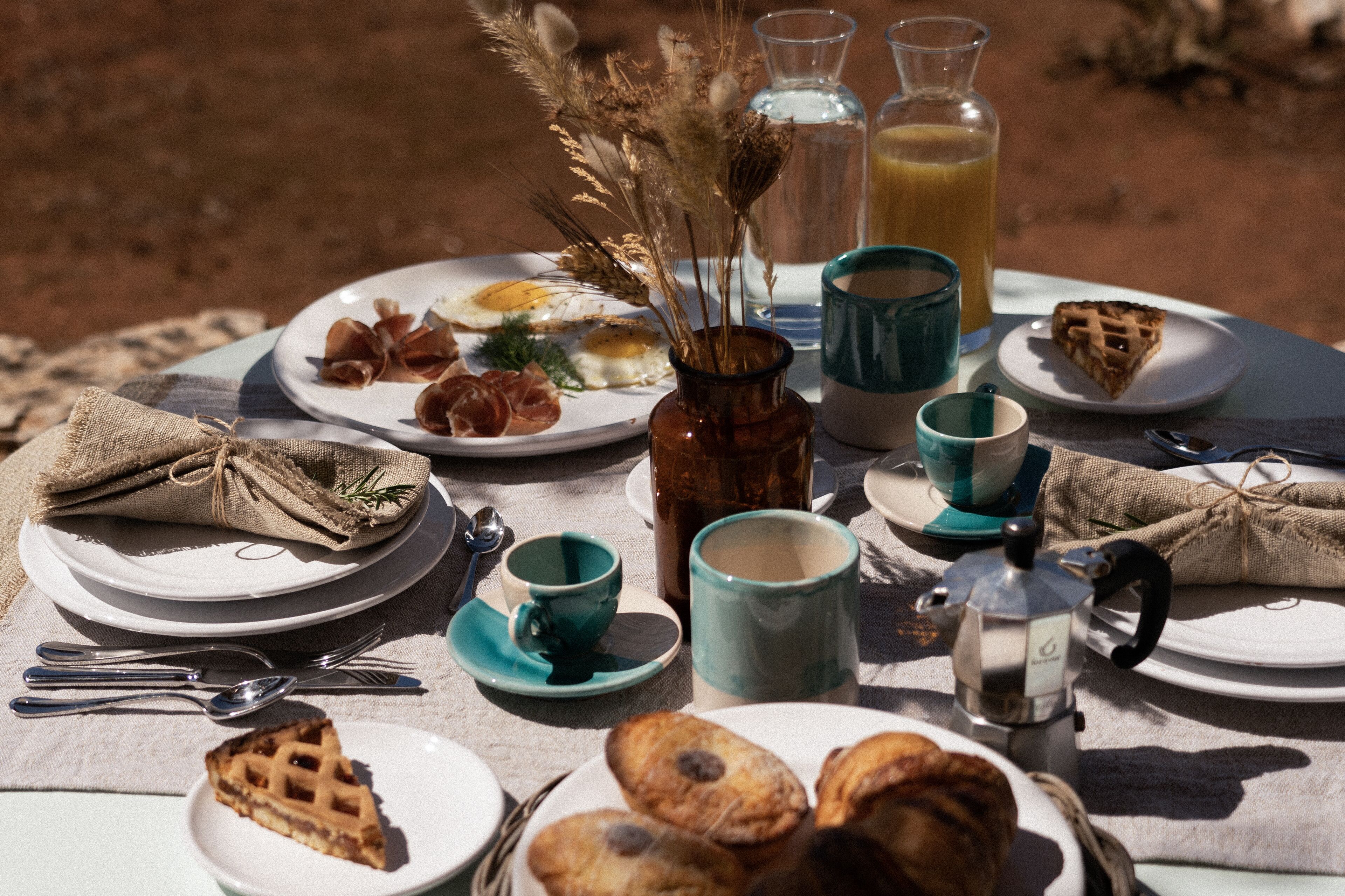 A table set for breakfast with plates of food, cups, and a coffee pot.