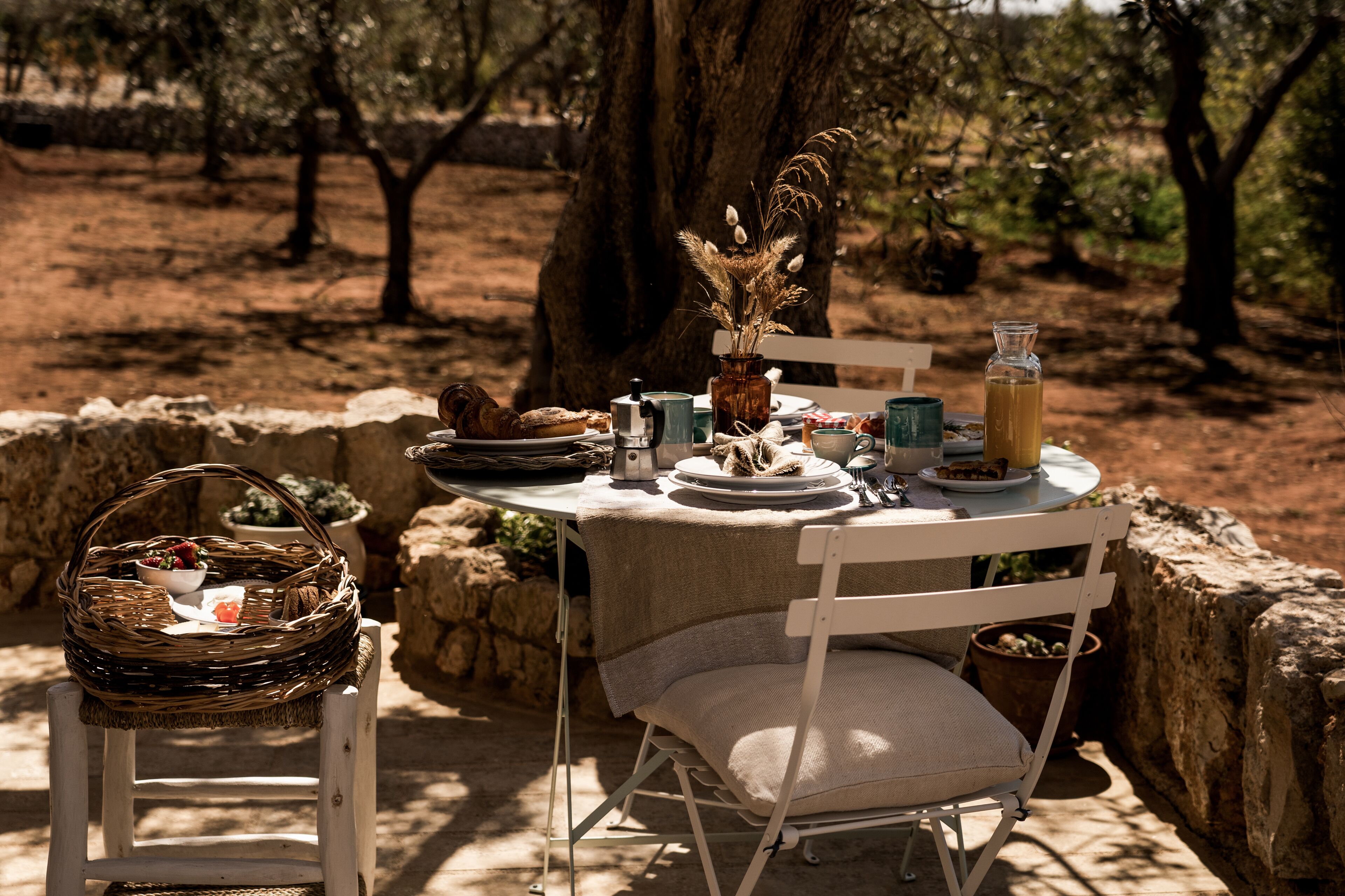 An outdoor dining setup with a table set for two, surrounded by stone walls and trees.