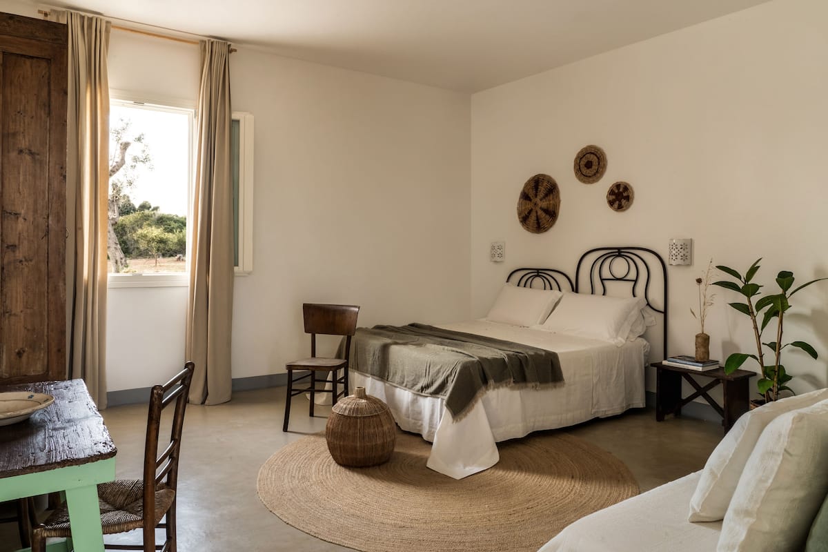 A bedroom with a bed, a chair, a table, and a window.
