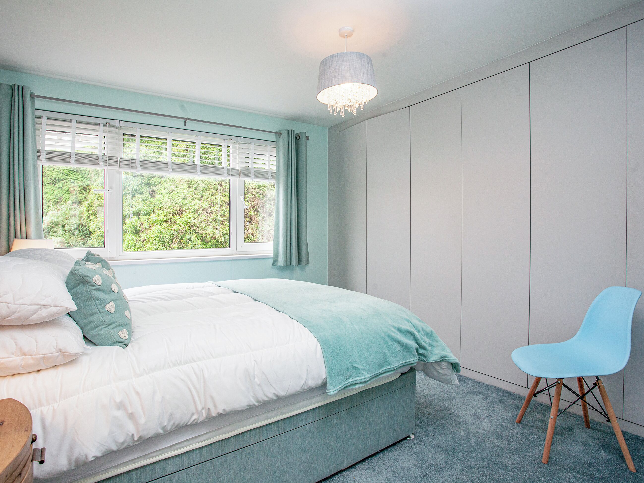 A bedroom with a bed, a chair, a window with curtains, and a wardrobe.