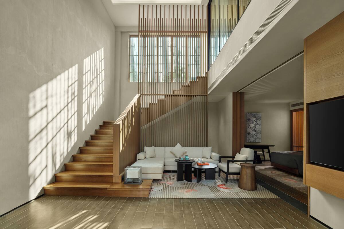 A modern living room with a staircase, a sofa set, a coffee table, and a flat-screen TV.