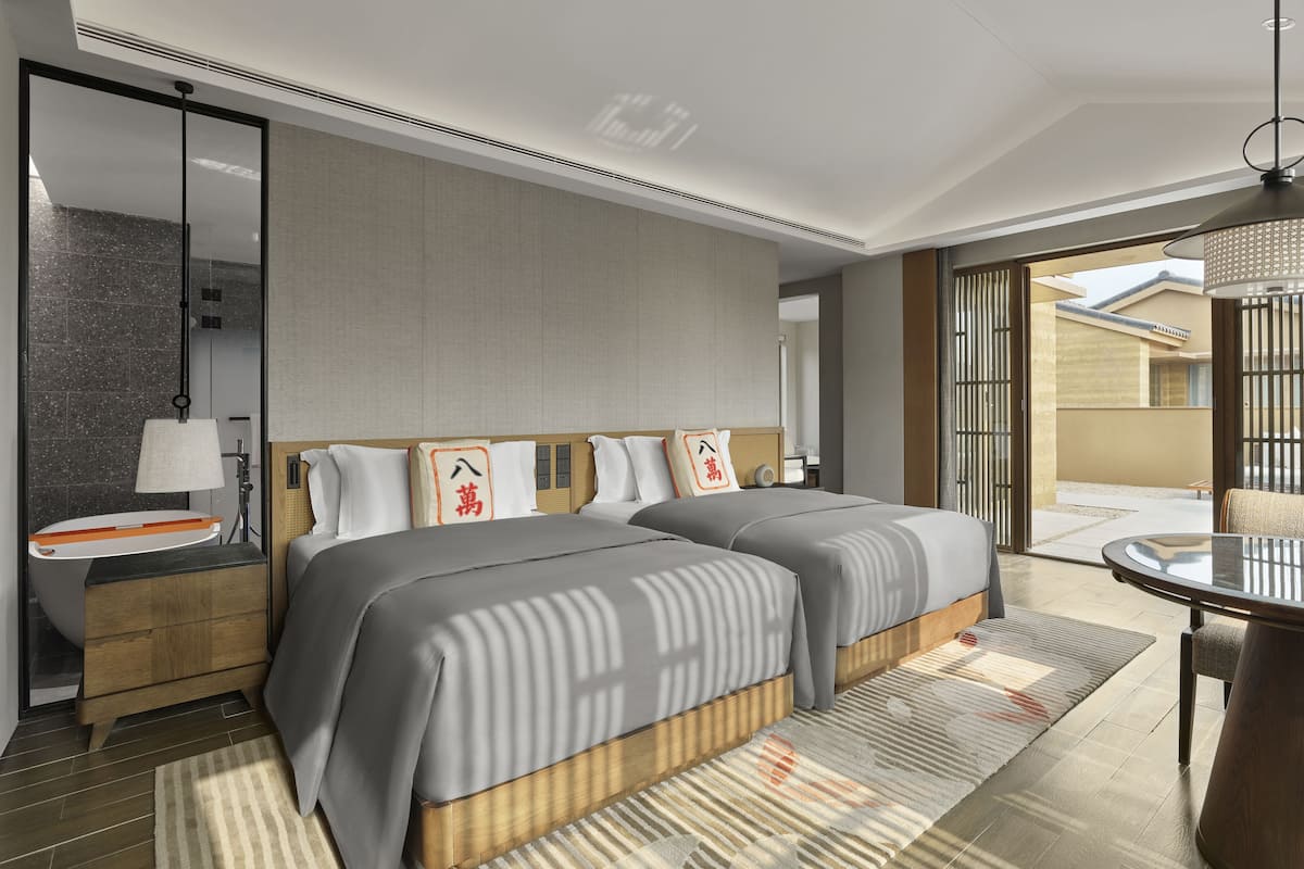 A modern hotel room with a large bed, a bedside table, a mirror, and a view of the outside.