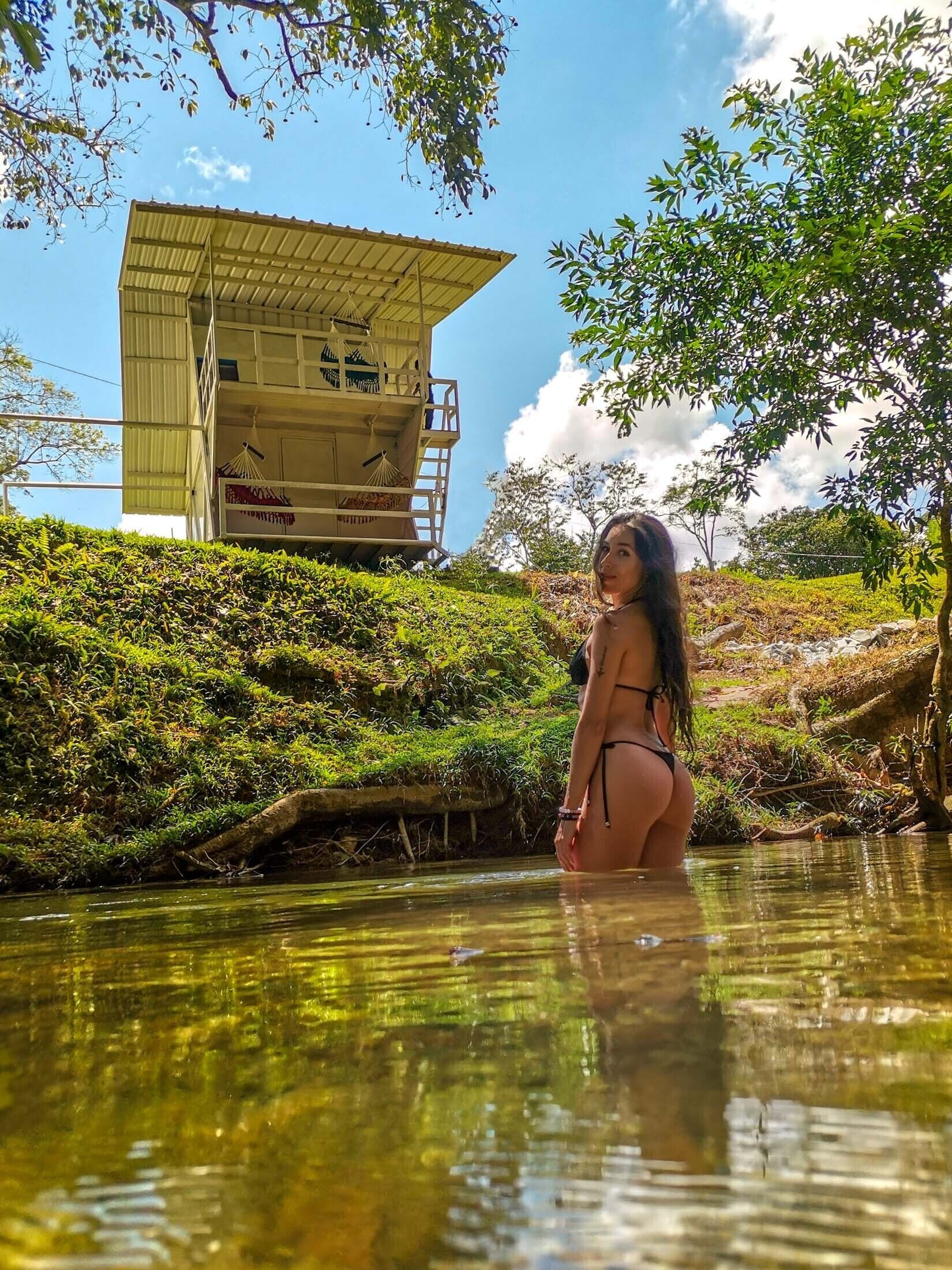 Eine Frau in einem Bikini steht in einem natürlichen Pool, im Hintergrund ein Gebäude.