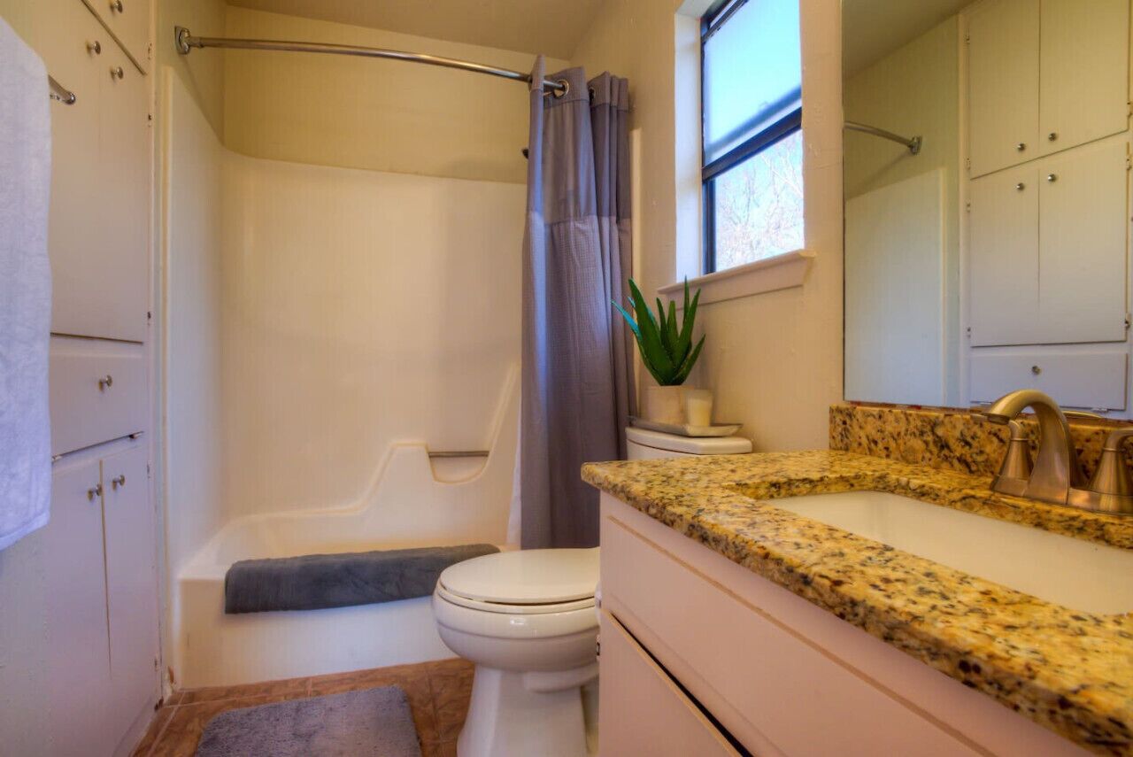 A bathroom with a bathtub, toilet, and a granite countertop sink.