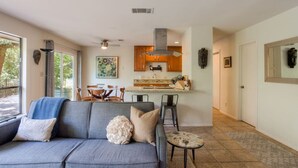 A modern living room with a grey sofa, a small round table, and a kitchen area with wooden cabinets and a stainless steel range hood. - Greenbelt Access & Views, Close to DT (Austin)
