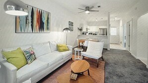 Uma sala de estar com sofá branco, mesa de centro redonda de madeira e um espaço de jantar com cadeira e mesa.