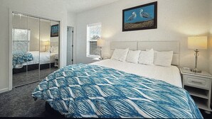 Quarto de hotel com uma cama grande, uma mesa de cabeceira, um abajur, um espelho e um quadro na parede.