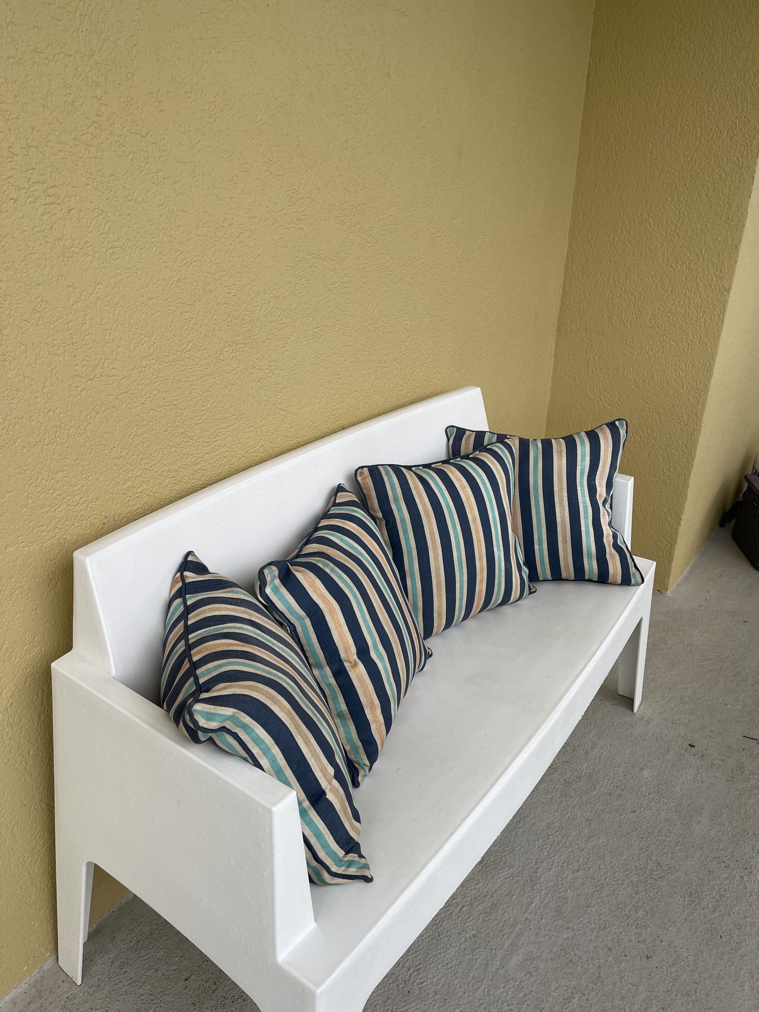 A white bench with striped cushions against a yellow wall.