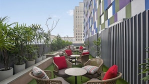 A rooftop terrace with wicker furniture, small round tables, and potted plants. - Ibis Kolkata Rajarhat (Barasat)