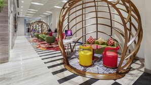 A modern lobby with a central seating area featuring a unique spherical wooden structure, surrounded by colorful chairs and a small table. - Ibis Kolkata Rajarhat (Barasat)