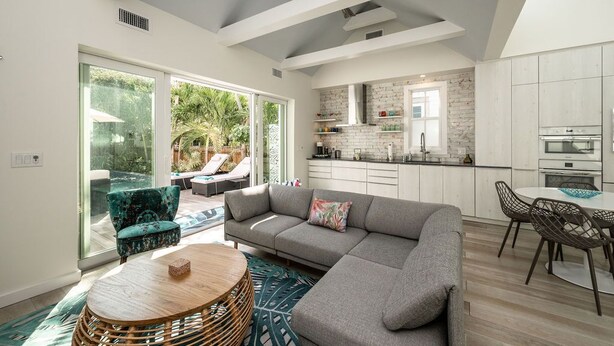 A modern living room with a grey sectional sofa, a round wooden coffee table, and a dining area with a white table and dark chairs. - THE CLASSY CONCH- Old Town Key West (Key West)
