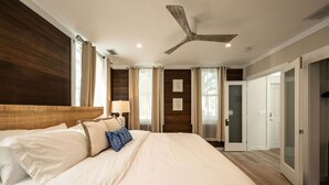 A spacious bedroom with a large bed, wooden paneling on the walls, a ceiling fan, and a door leading to another room. - THE CLASSY CONCH- Old Town Key West (Key West)