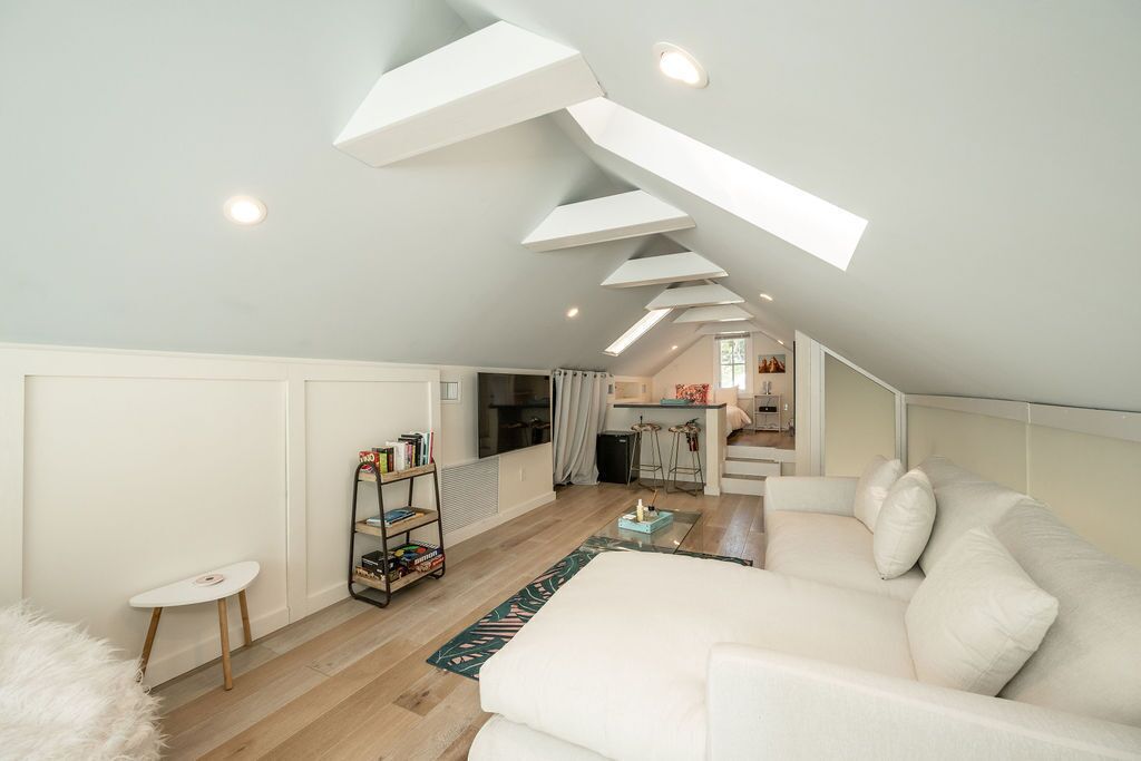 A modern loft apartment with a high ceiling, white walls, a white sofa, a small table, and a bookshelf.