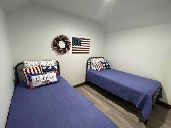 Ein Zimmer mit zwei Betten, jeweils mit blauer Bettdecke und Kissen mit amerikanischer Flagge-Motiv.