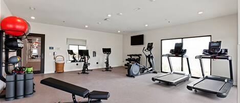 Une salle de sport moderne équipée de divers appareils d’exercice, notamment des tapis de course, un vélo elliptique et un banc de musculation.