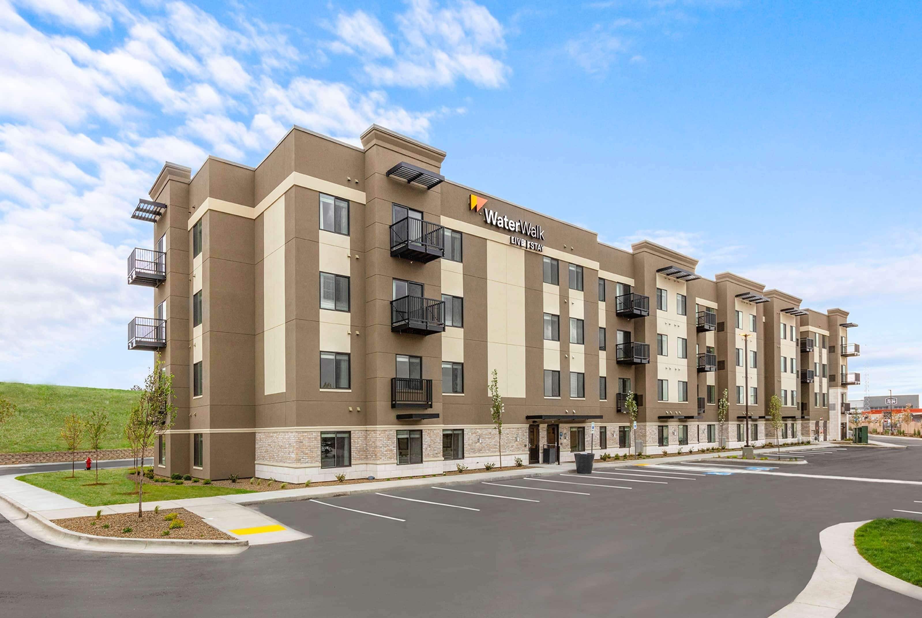 A multi-story hotel with a flat roof, balconies, and a parking lot in front.