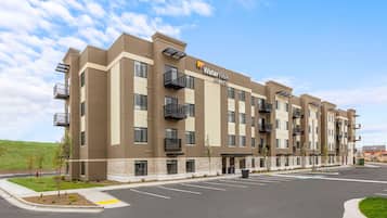 A multi-story hotel with a flat roof, balconies, and a parking lot in front.