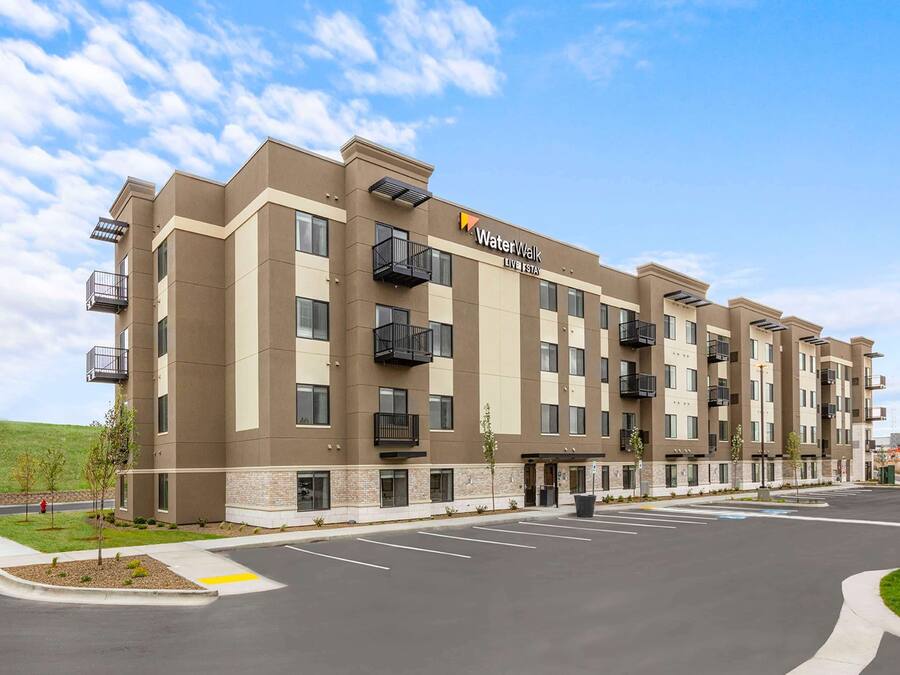 A multi-story hotel with a flat roof, balconies, and a parking lot in front.