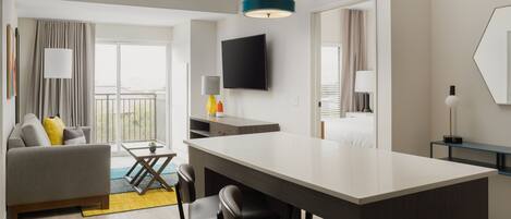 Una habitación de hotel moderna con comedor, sofá, televisión y un ventanal grande.