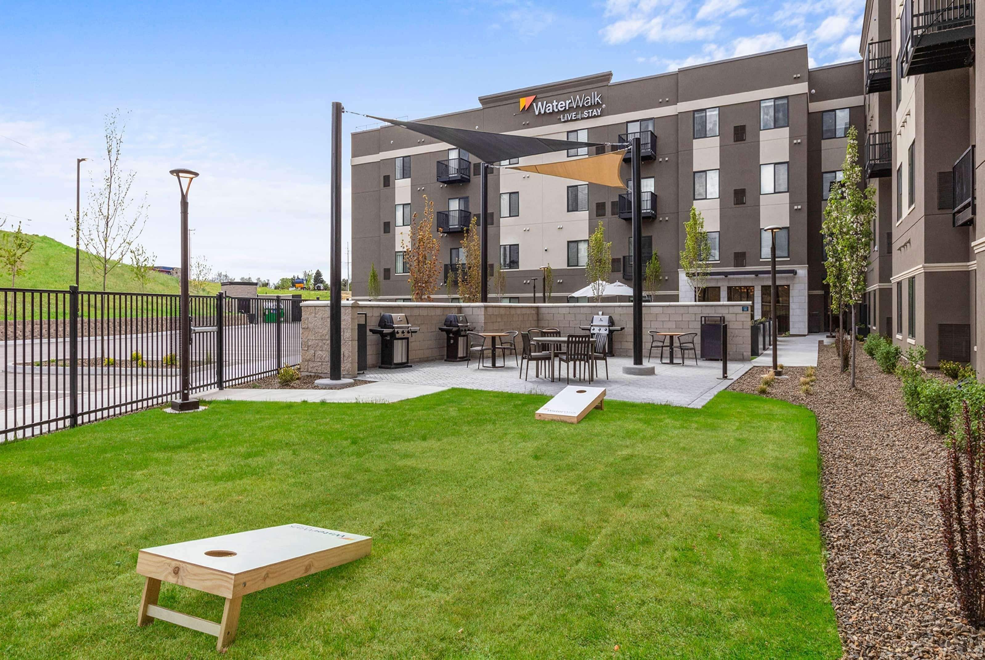 A courtyard with a wooden board game, outdoor seating, and a building labeled "WaterWalk Live Stay".
