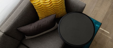 A modern living room with a grey sofa, a yellow textured pillow, a dark pillow, and a round black side table.
