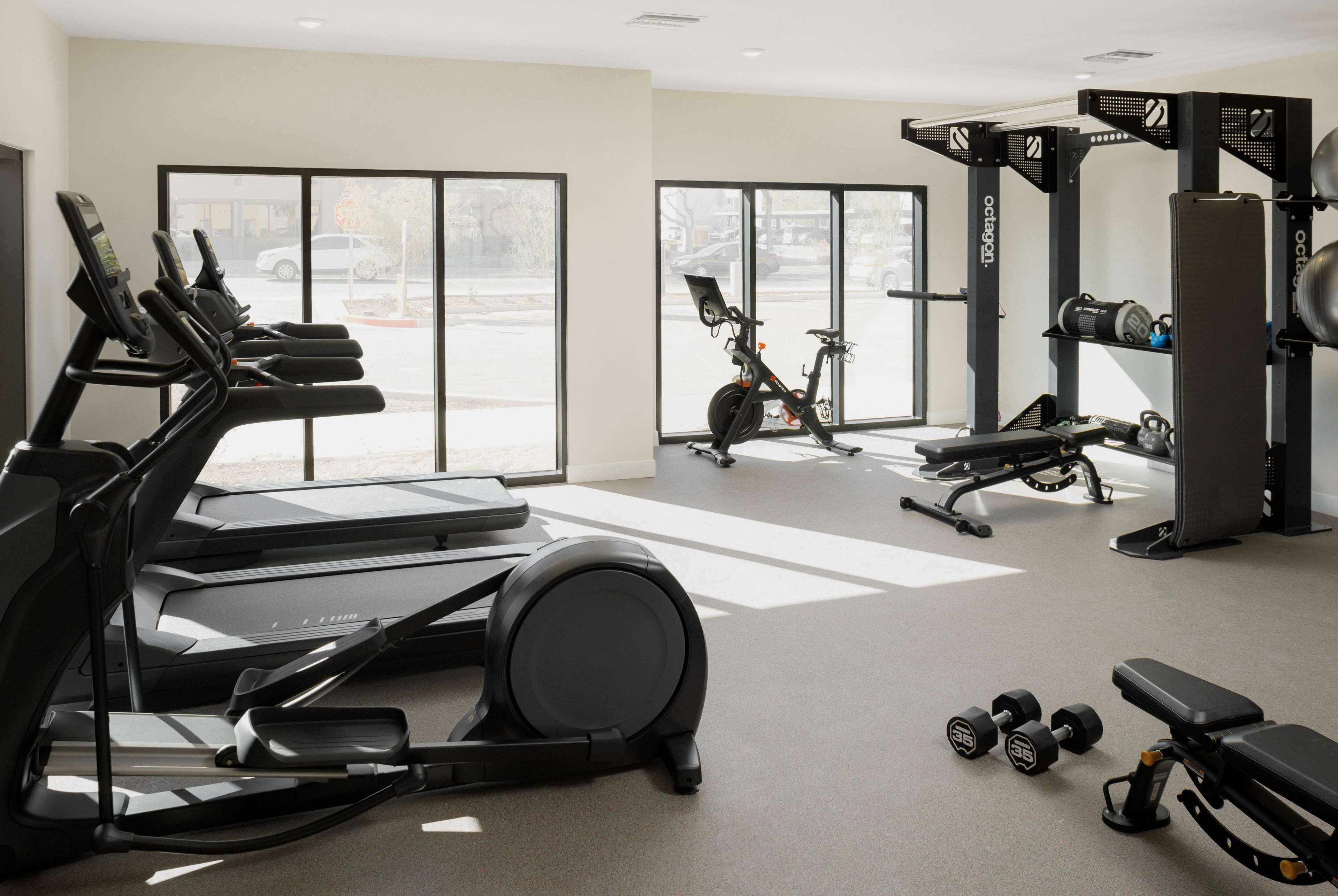 A gym with treadmills, an elliptical, a stationary bike, a bench, dumbbells, and a weight machine.