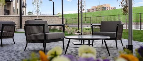Une terrasse extérieure avec deux tables rondes et quatre chaises, entourée d’une clôture et avec un bâtiment en arrière-plan.