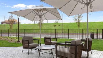 Eine Terrasse im Freien mit Sitzgelegenheiten und Sonnenschirmen, ein sanfter Hügel im Hintergrund und ein Zaun.