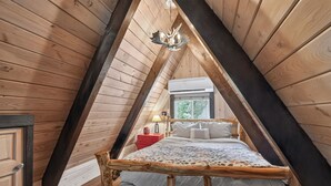Ein Schlafzimmer im Dachgeschoss mit Holzboden, einem Bett, einem Nachttisch und einem Fenster.