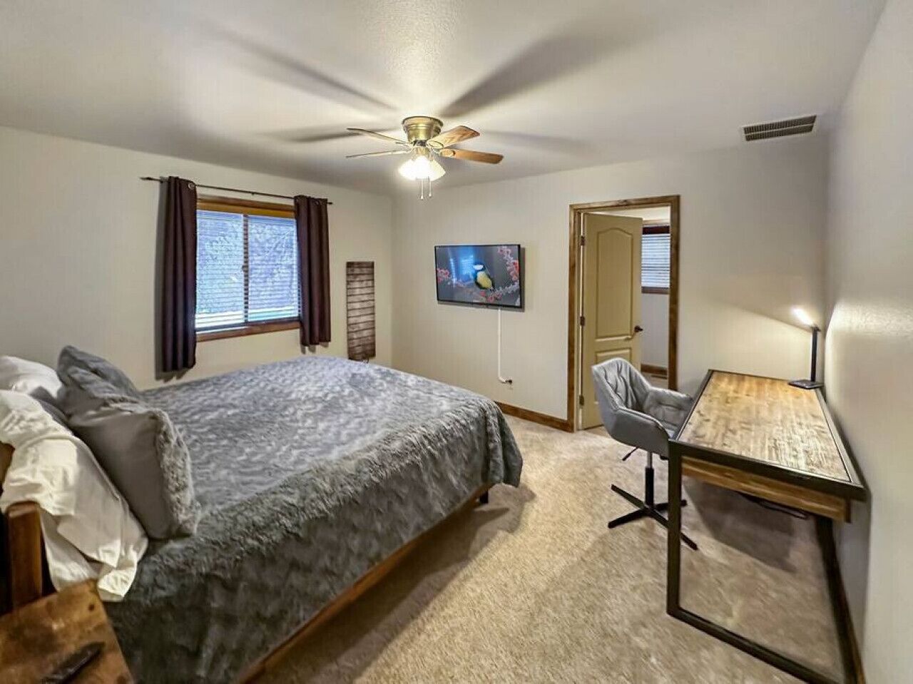 Ein Schlafzimmer mit einem Bett, einem Schreibtisch, einem Stuhl, einem Deckenventilator, einem Fernseher und einer Tür.