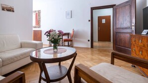 Un salon comprenant un canapé, une table ronde ornée d’un vase de fleurs, un meuble en bois et un téléviseur.