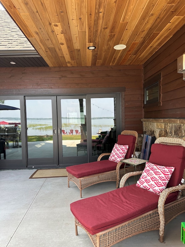 A covered patio area with wicker lounge chairs and a stone fireplace.