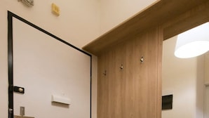 A hallway with a door, a wooden panel wall, a mirror, and a light fixture. - Quiet Studio by Anděl Metro - Walk to Old Town, Next to Nový Smíchov Mall (Prague)