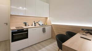 A modern kitchen with white cabinets, a built-in oven, a sink, and a wooden countertop. There is a dining area with a table and chairs. - Quiet Studio by Anděl Metro - Walk to Old Town, Next to Nový Smíchov Mall (Prague)