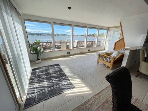 Enjoy a serene view of the water from this room's large window, featuring a comfortable chair and a potted plant.