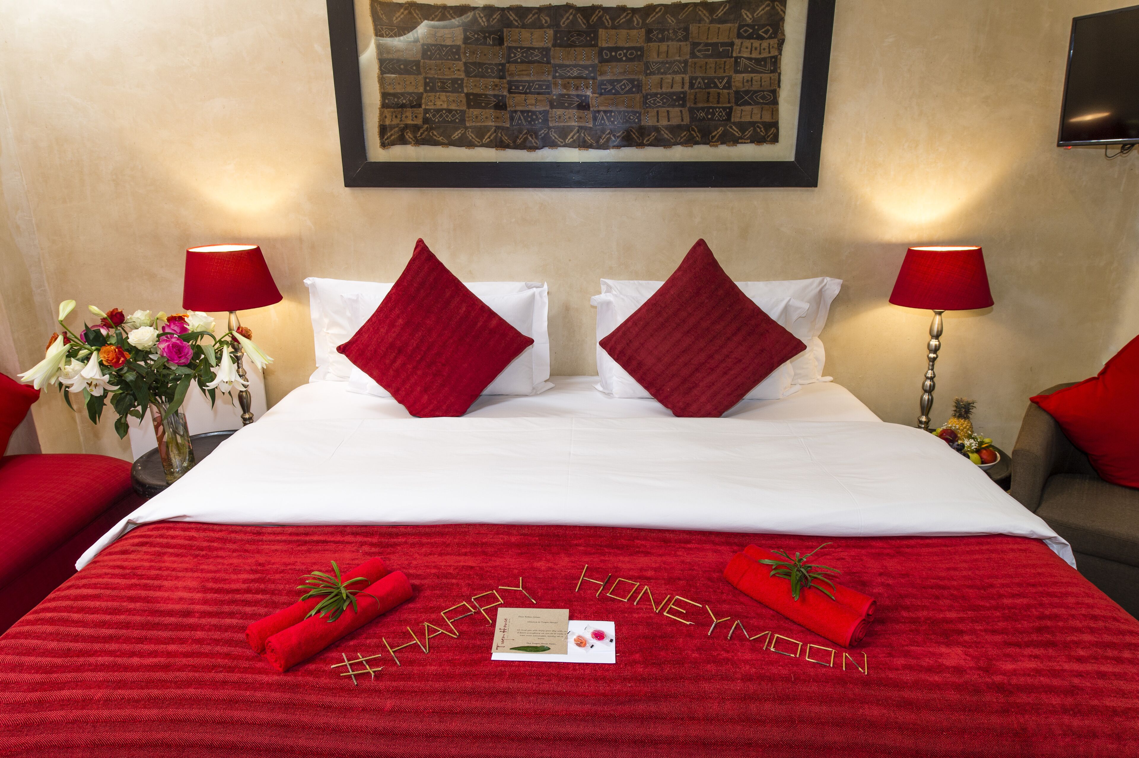 Una habitación de hotel con una cama bien hecha, almohadas rojas y una colcha roja con la frase 'HAPPY HONEYMOON' escrita.