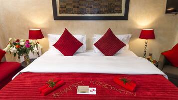 A hotel room with a neatly made bed, red pillows, and a red bedspread with the words "HAPPY HONEYMOON" written on it.