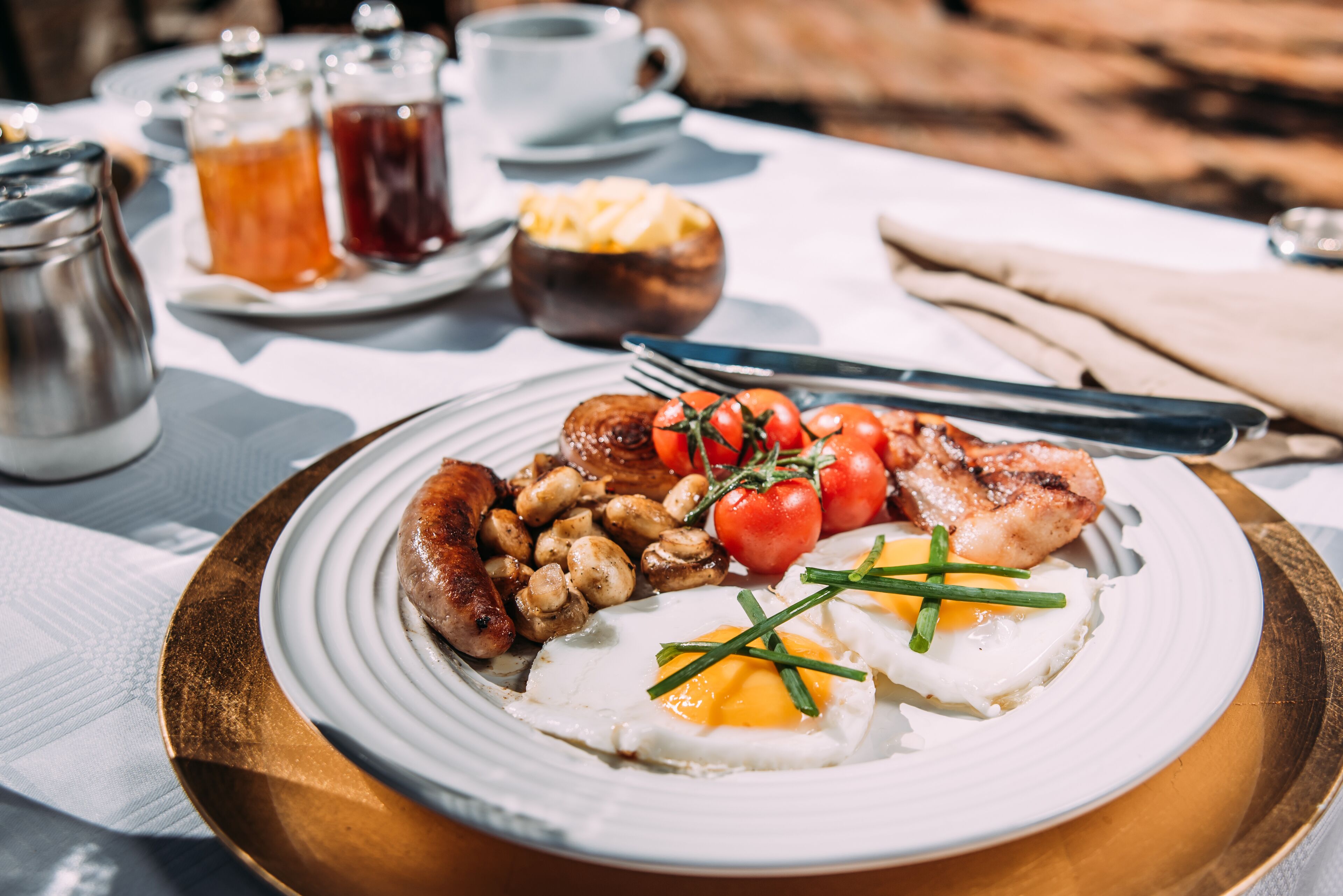 Un plato de desayuno con huevos, salchichas, champiñones, tomates y cebollines.