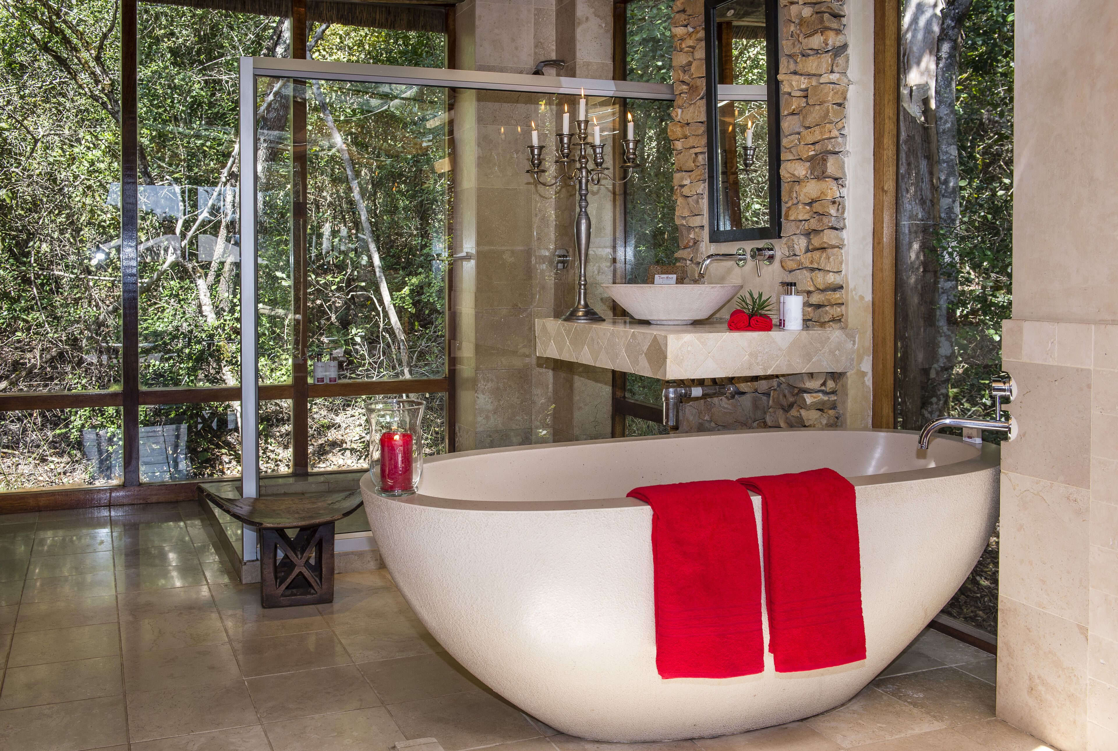 A modern bathroom with a freestanding bathtub, a glass shower enclosure, and a large window offering a view of trees.