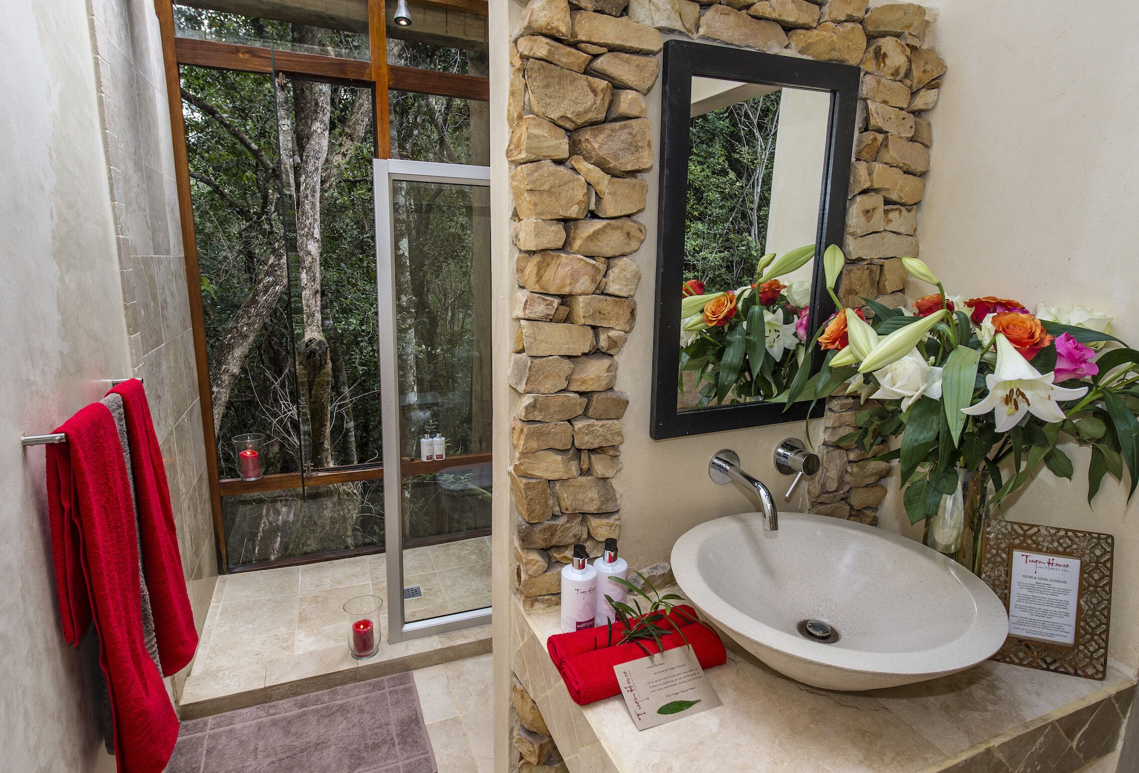 Un baño con pared de piedra, un ventanal grande, un lavamanos y un espejo.
