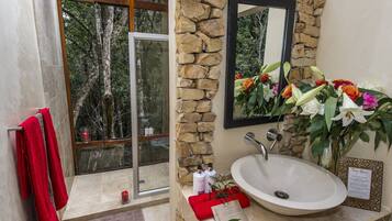 Un baño con pared de piedra, un ventanal grande, un lavamanos y un espejo.