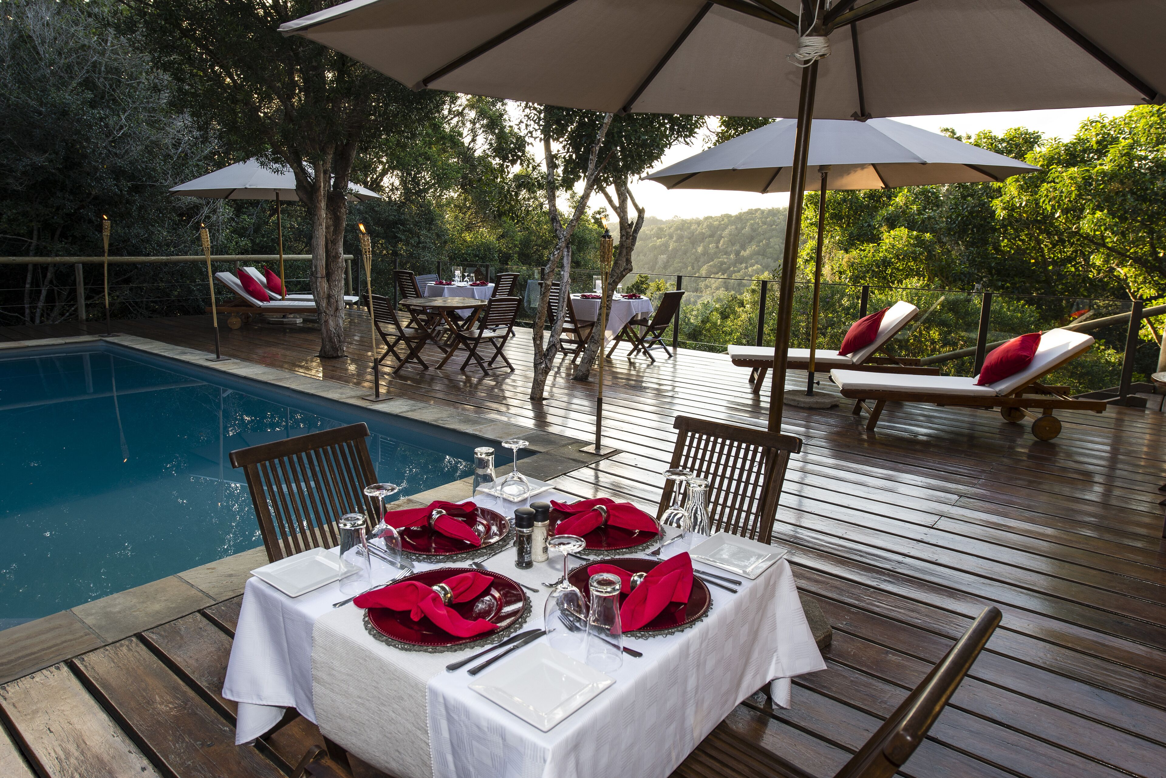 Un espace repas avec des tables dressées pour le dîner, donnant sur une piscine et une végétation luxuriante.