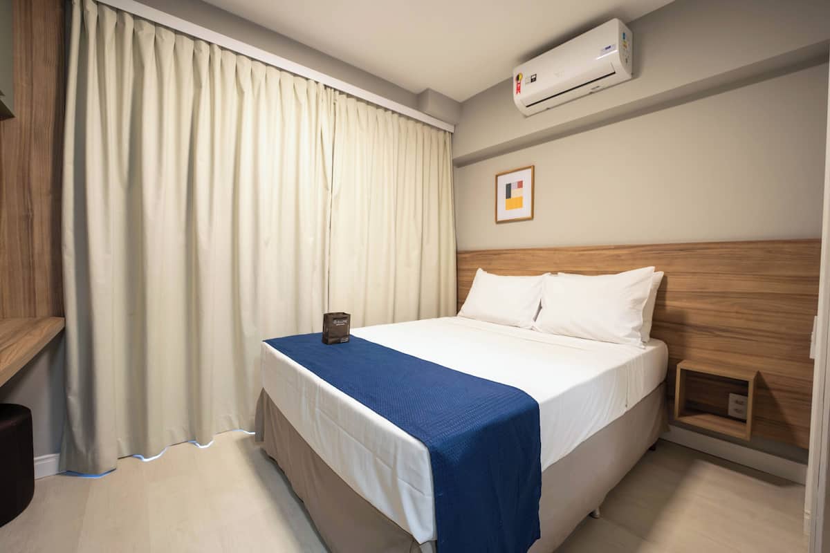 Una cama bien hecha con cubrecama azul, cabecera de madera y almohada blanca.