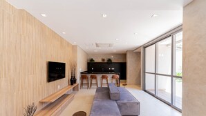 A modern living room with a TV, seating area, and kitchen in the background. - Apartamentos Studio Allure Moema (São Paulo)
