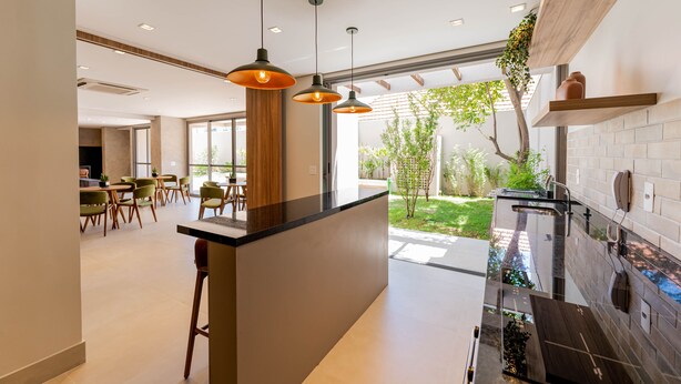 A modern kitchen with pendant lighting, a central island, and a view of the outdoor garden. - Apartamentos Studio Allure Moema (São Paulo)