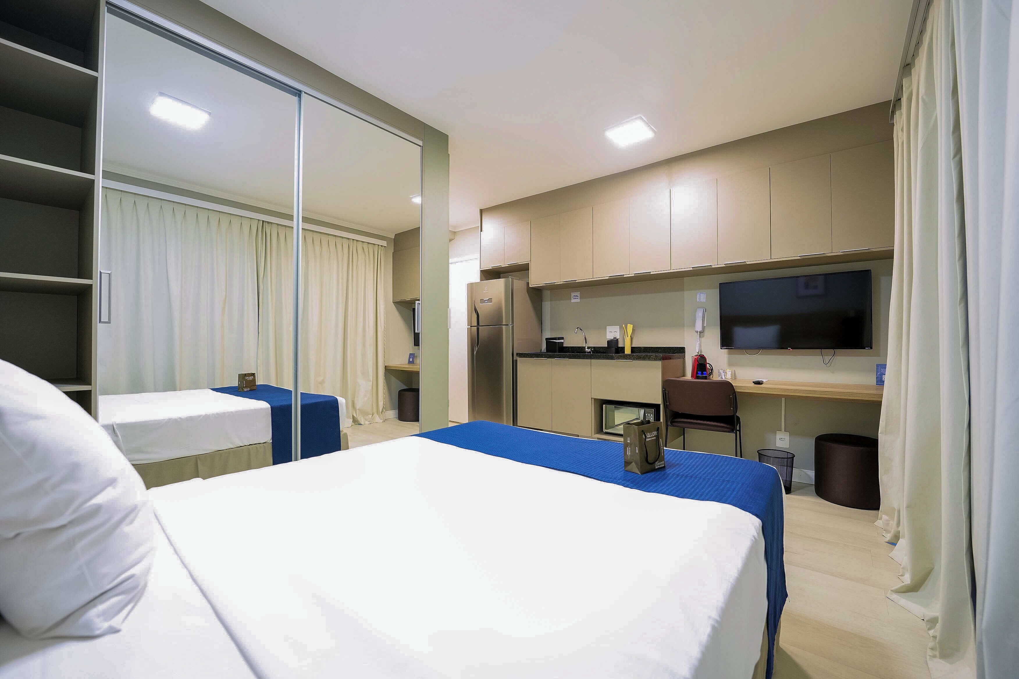 A hotel room with a bed, a desk, a television, and a kitchenette.