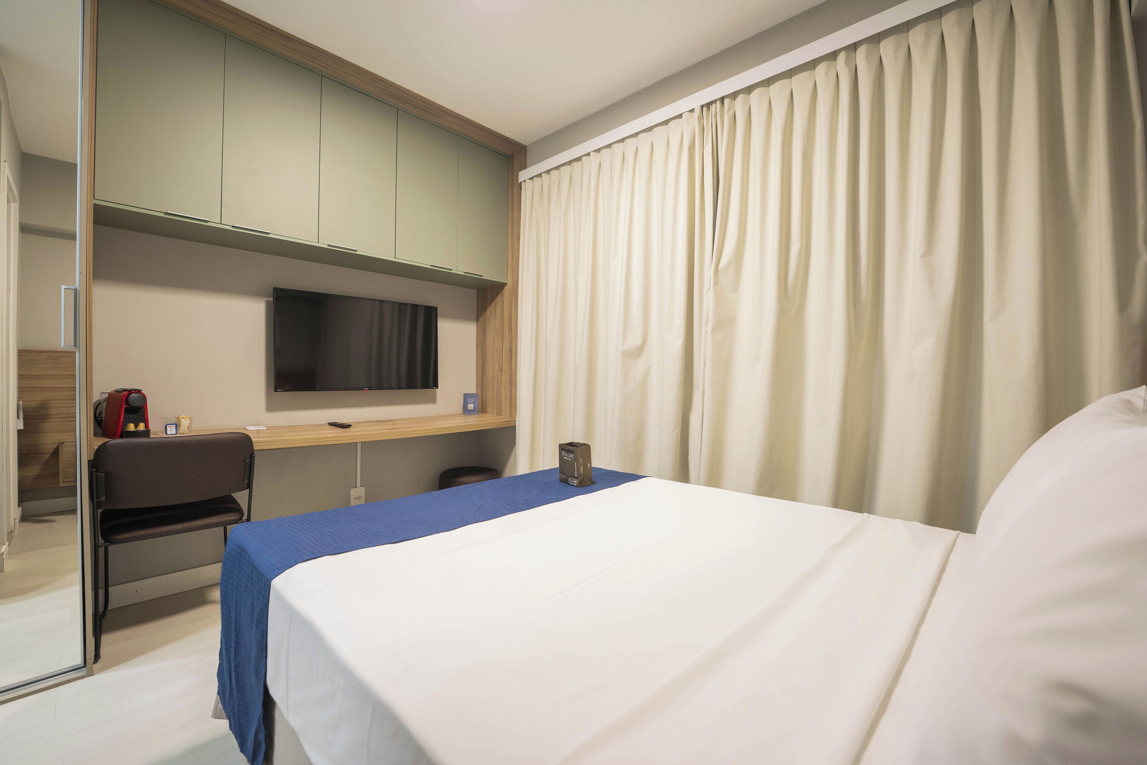 A hotel room with a bed, a desk, a chair, a television, and a window with curtains.
