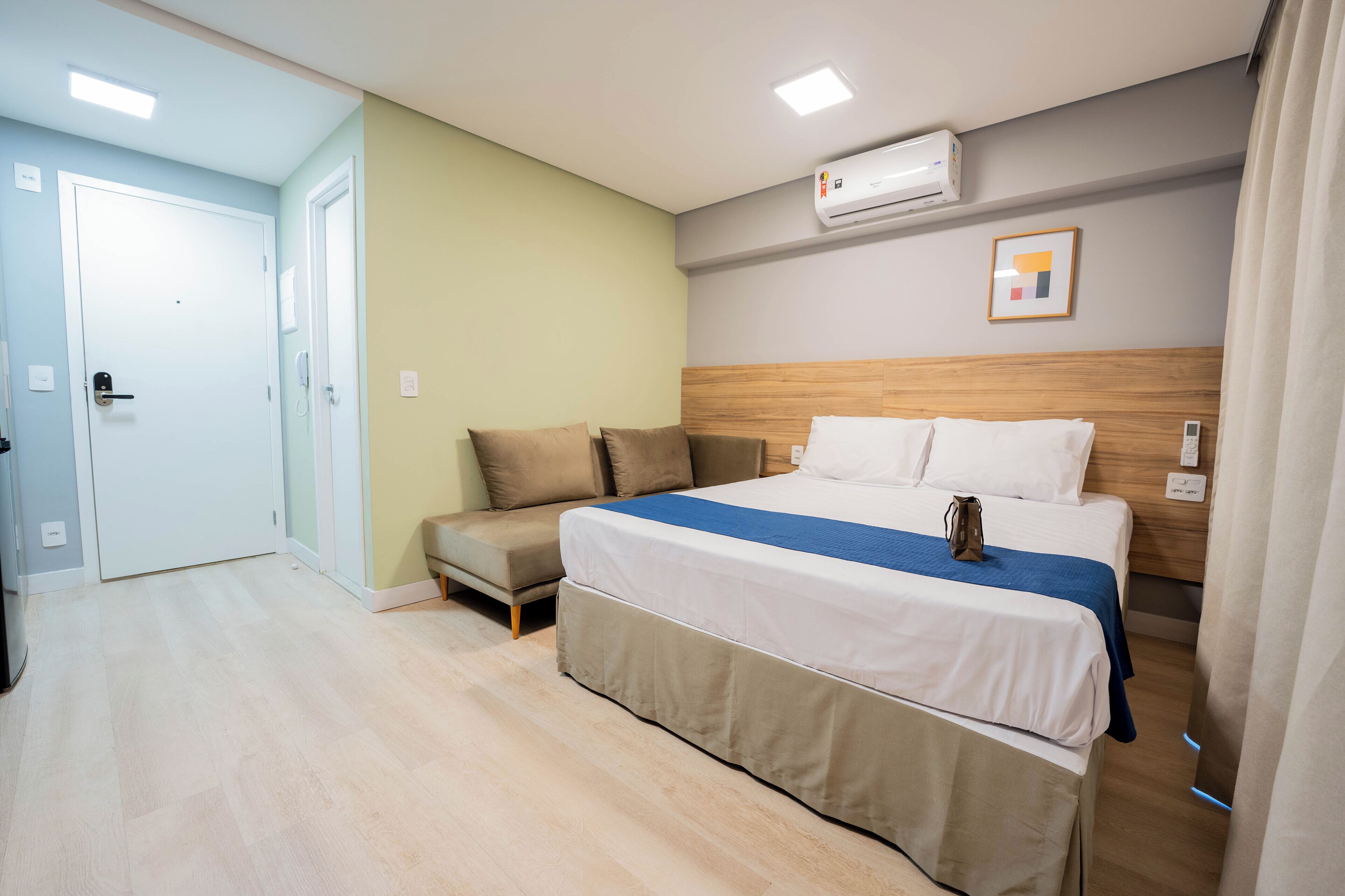 Une chambre d’hôtel comprenant un lit, un canapé, une tête de lit en bois, un appareil de climatisation et une porte.