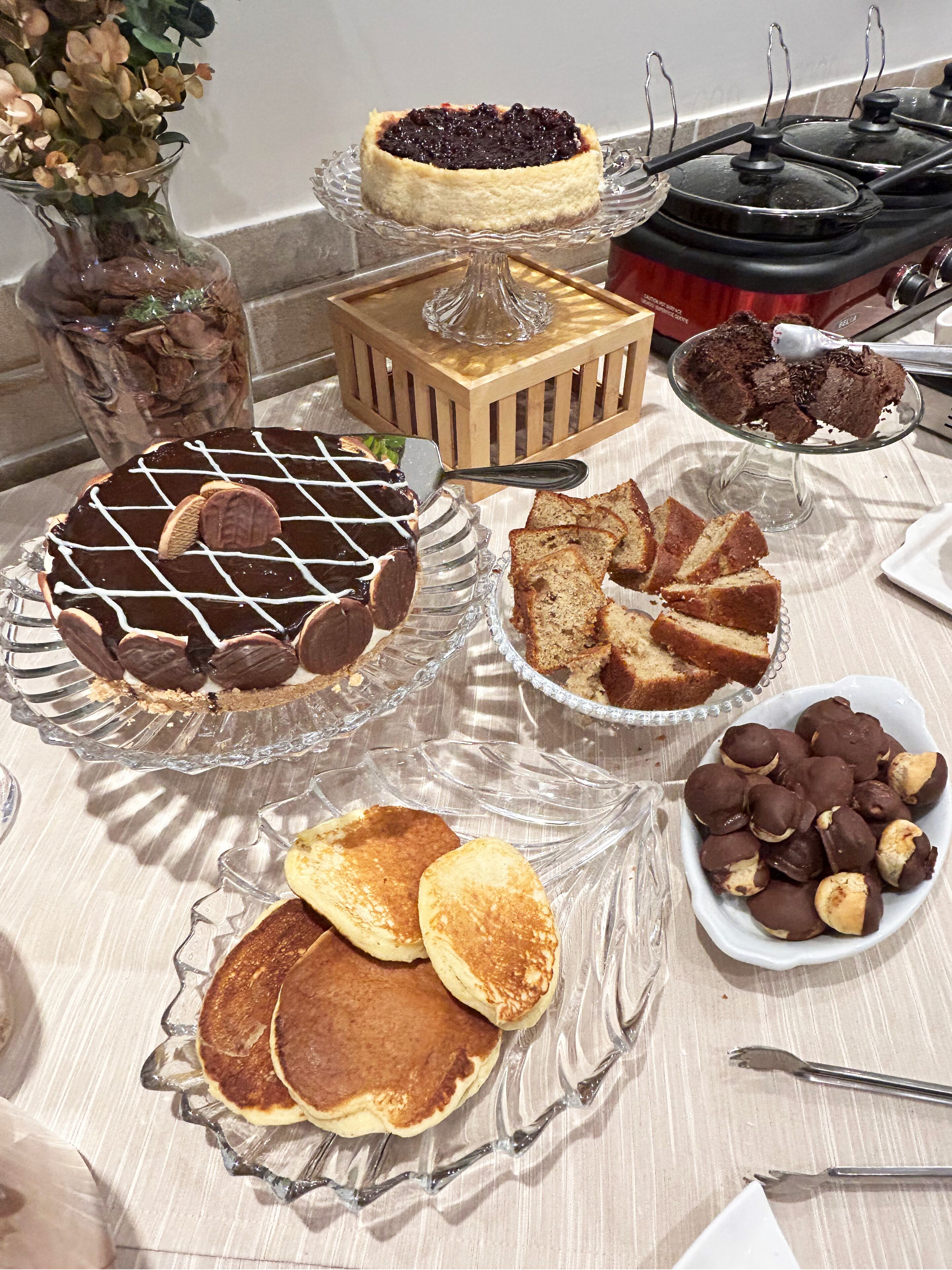 A table with various desserts including a cheesecake, chocolate-covered cookies, and pancakes.